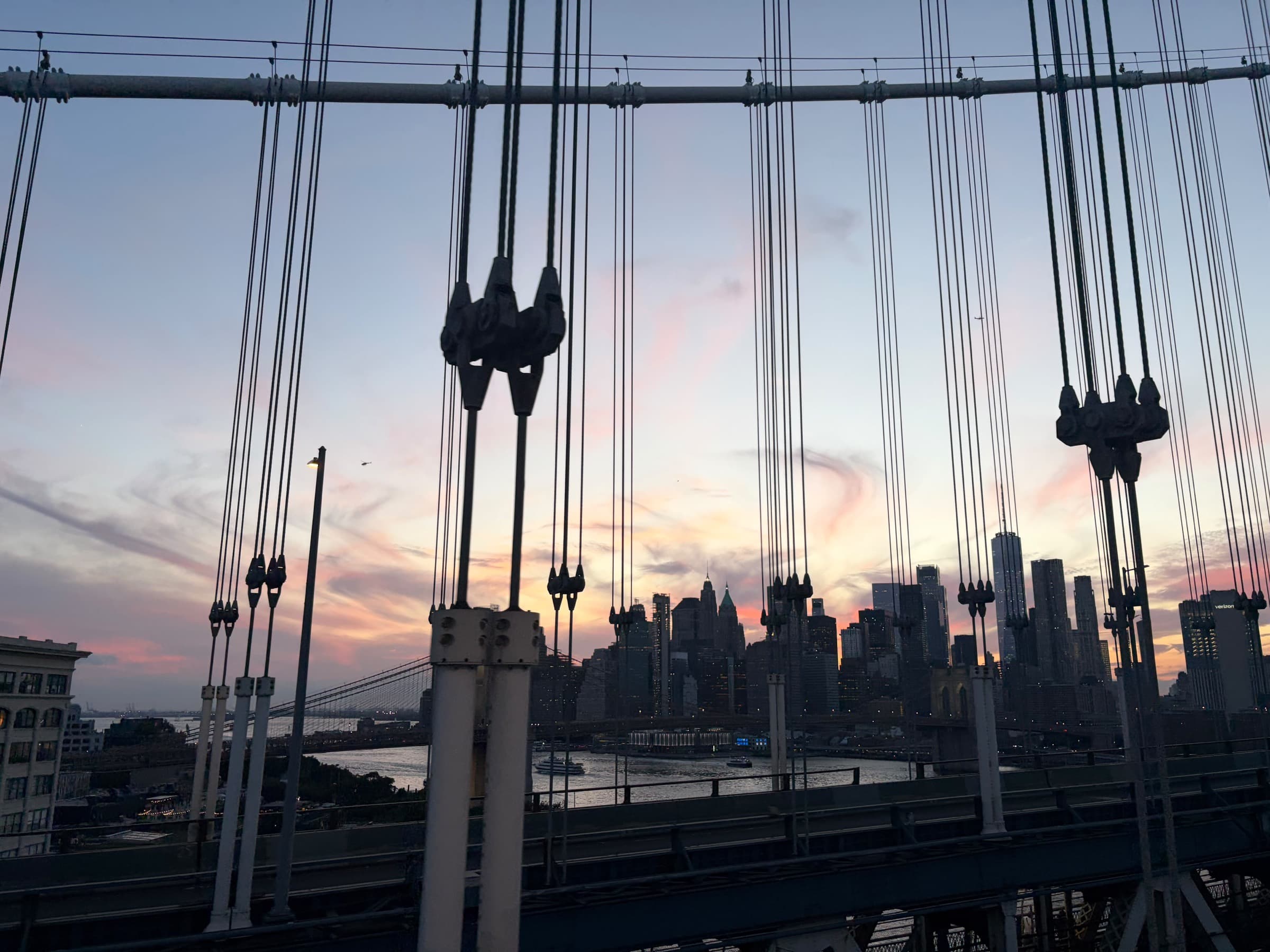 Manhattan at dusk seen through the cables and suspenders of the Brooklyn Bridge