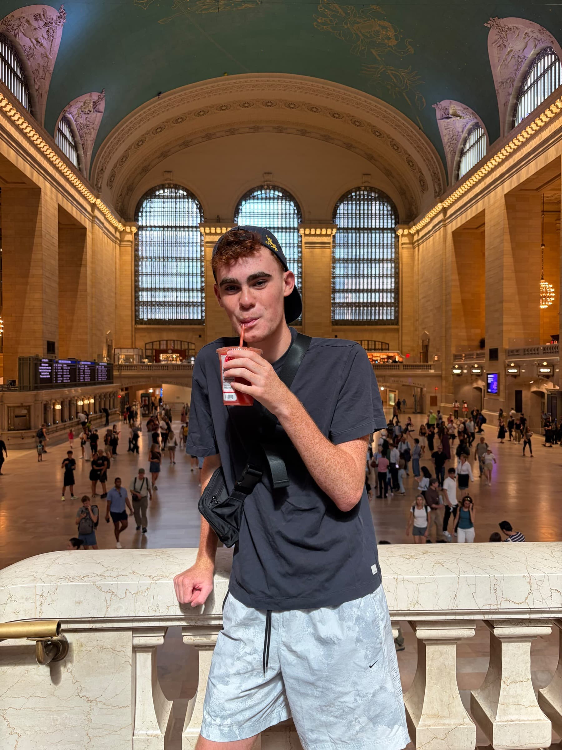 A young man drinking from a cup on the balcony of Grand Central Terminal