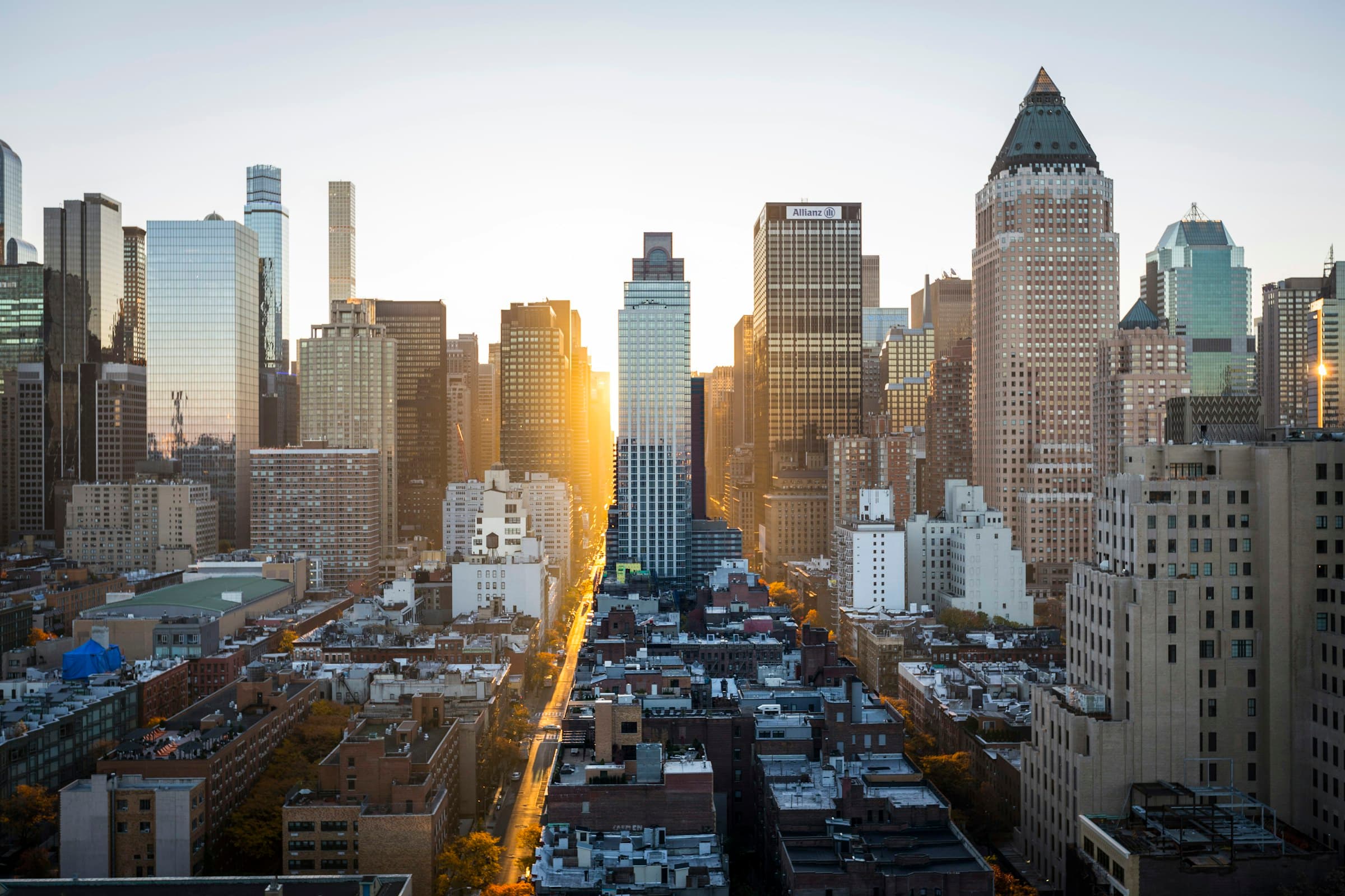 A sunlit Manhattan avenue seen from above, light running down the center of the grid