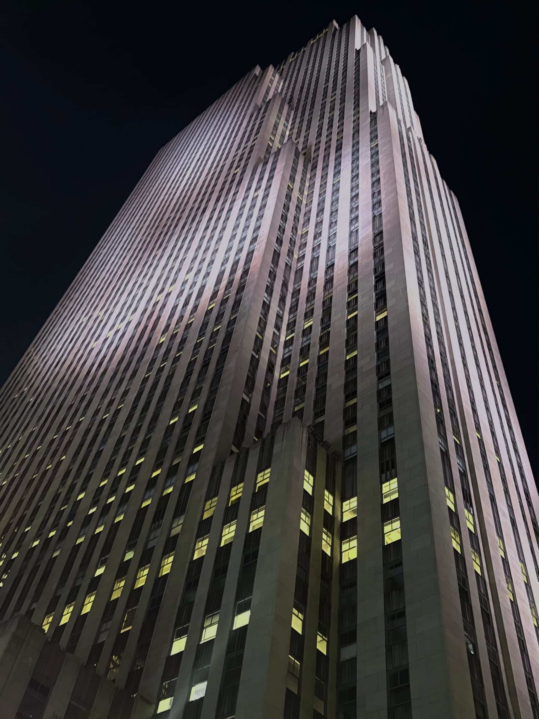The limestone facade of 30 Rockefeller Plaza at night with scattered yellow windows